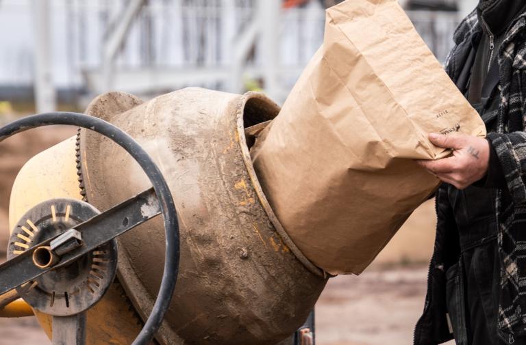 Hand håller i en cementsäck vid en cementblandare.